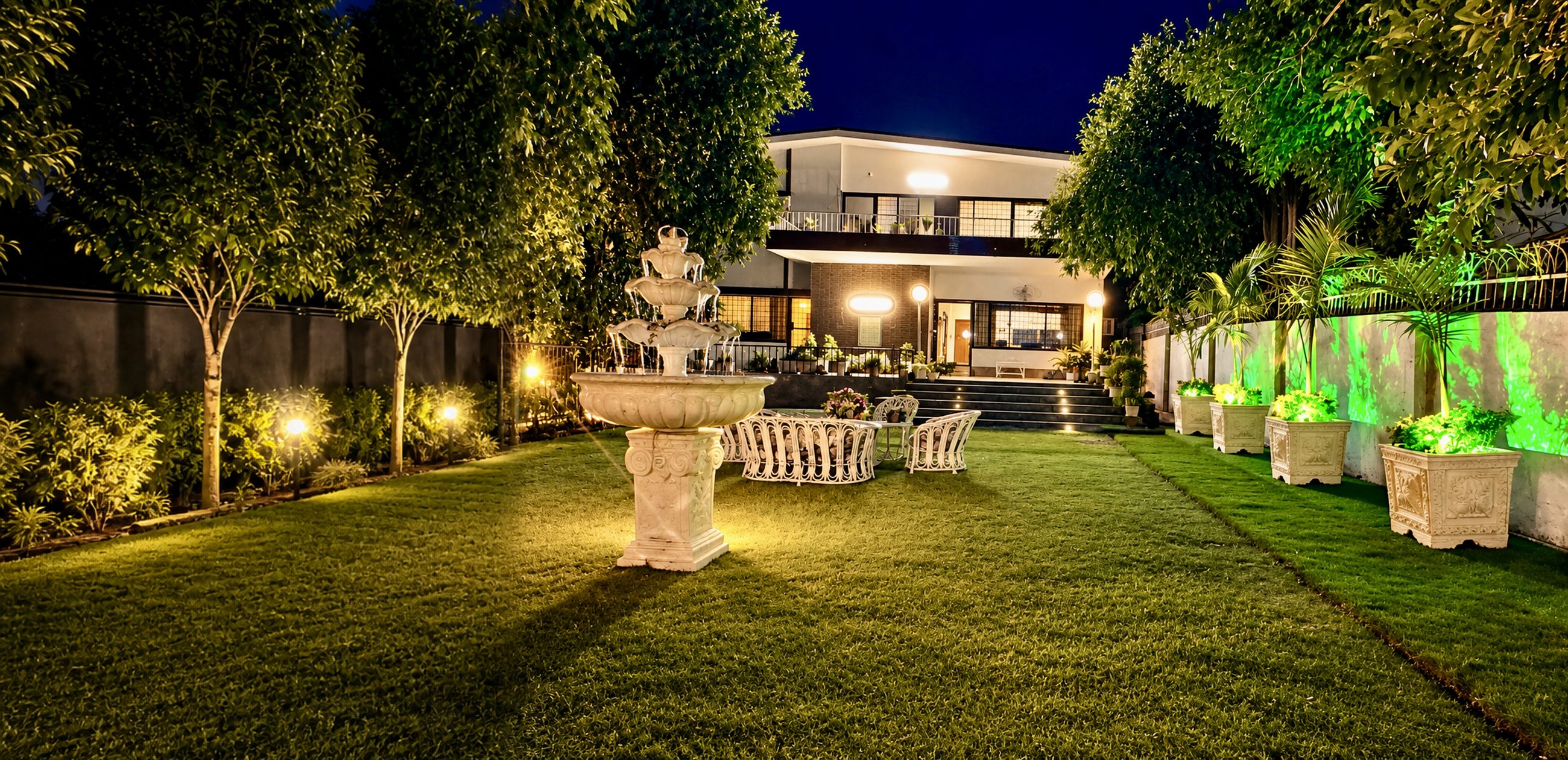 Baylis House lawn with fountain and garden seating, lit up at night